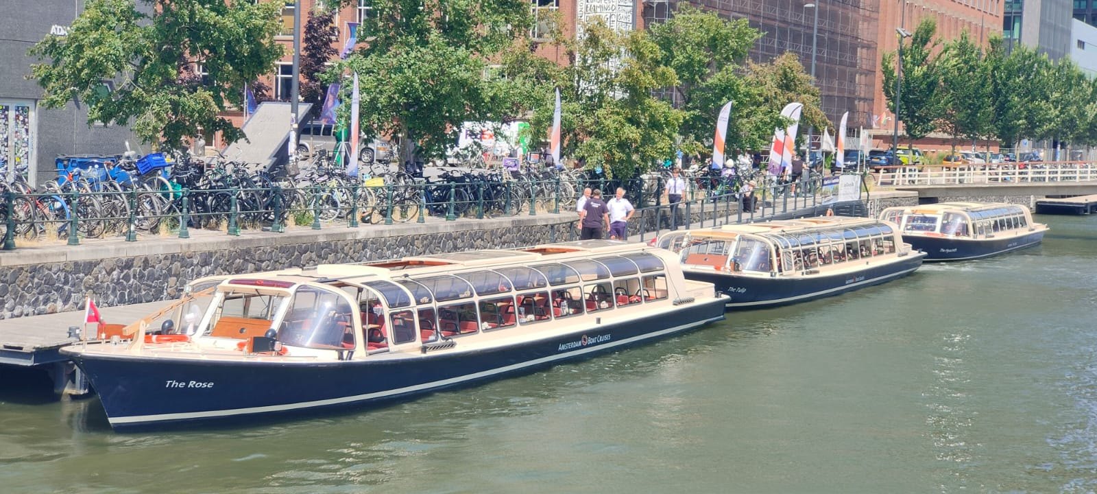 Drie schepen van Amsterdam Boat Cruises liggen achter elkaar aangemeerd.